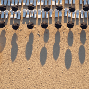 Aerial view of a sandy beach with rows of white sun loungers and black umbrellas